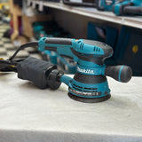 Side view of Makita BO5041 corded sander with dust bag attached